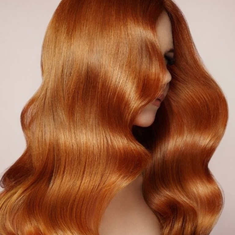 Eine Person mit langem, welligem, rötlichem Haar auf leichtem Hintergrund.