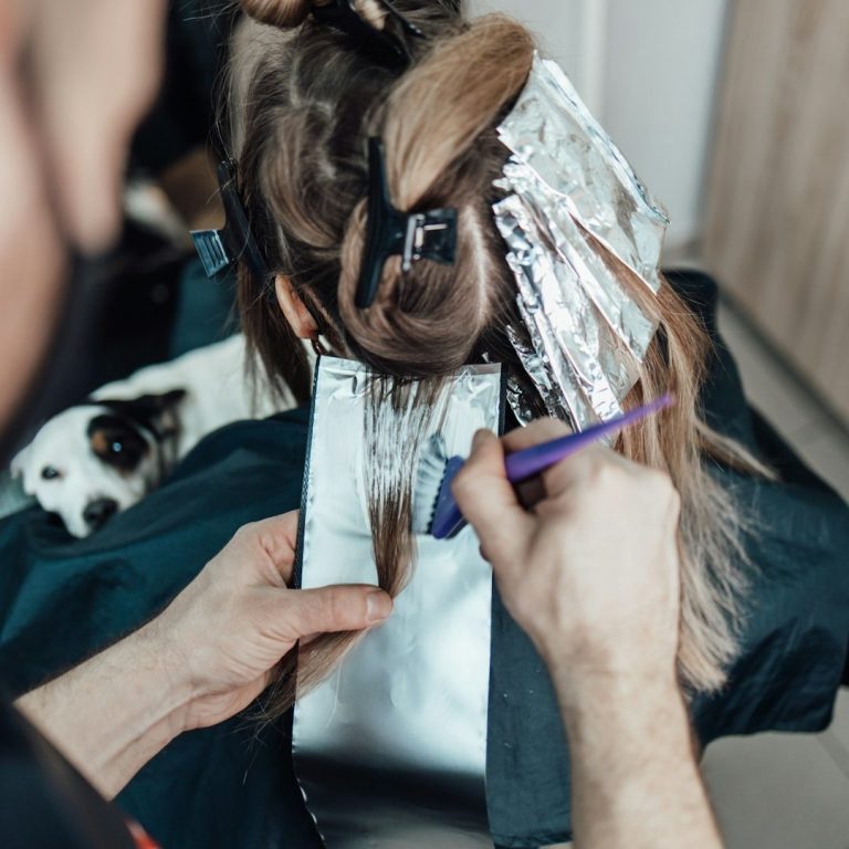 Friseur färbt Haare einer Kundin, während ein Hund auf dem Tisch sitzt.