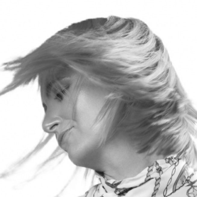 Frau mit wehenden Haaren, die seitlich mit einem nachdenklichen Ausdruck blickt.