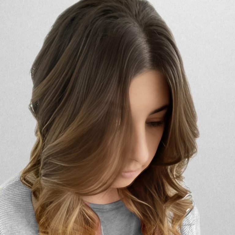 Haarfarbe 2026 Frau mit langen, welligen Haaren in grauem Oberteil, blickt nach unten.