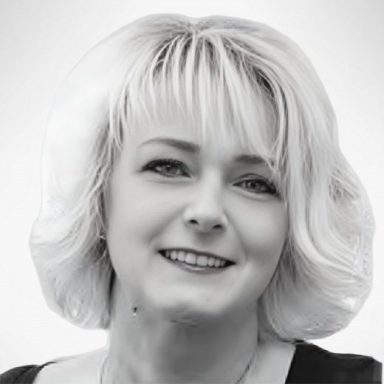 Claudia Rogalla Person mit blonden, lockigen Haaren lächelt freundlich in schwarz-weiß.